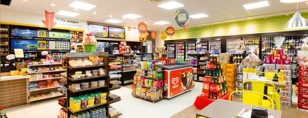 Loja de conveniência organizada, com gôndolas, geladeiras e caixa ao fundo